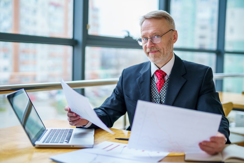 mature businessman looking laptop reading printed documents - Clés de succès pour Directeurs Financiers : compétences, défis et préparation au recrutement